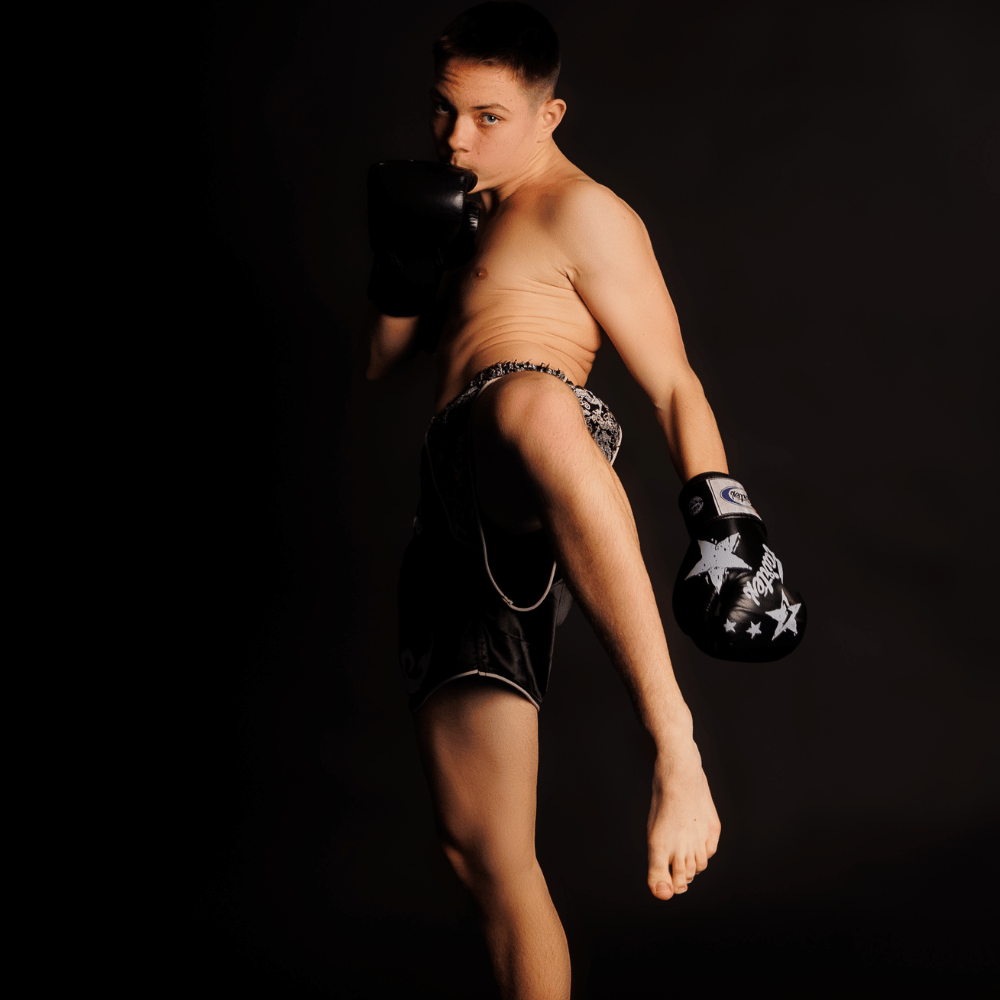 Chłopak w rękawicach bokserskich wyprowadzający kopnięcie kolanem - zawodnik Alpha Fight Club